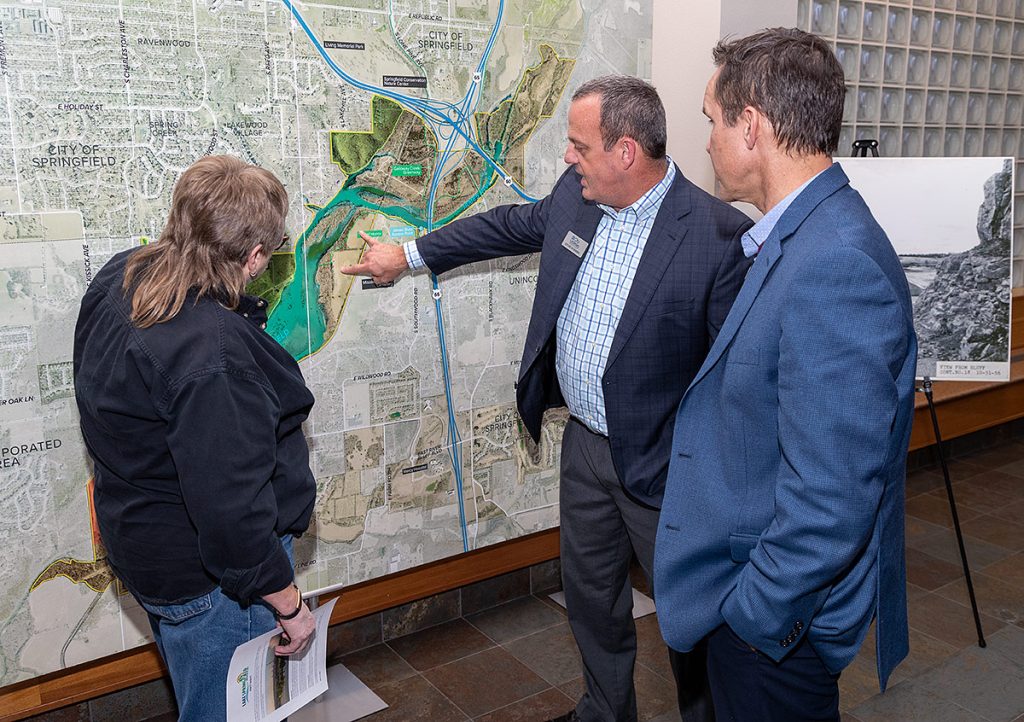 one man pointing out details on a giant map viewed by two other people